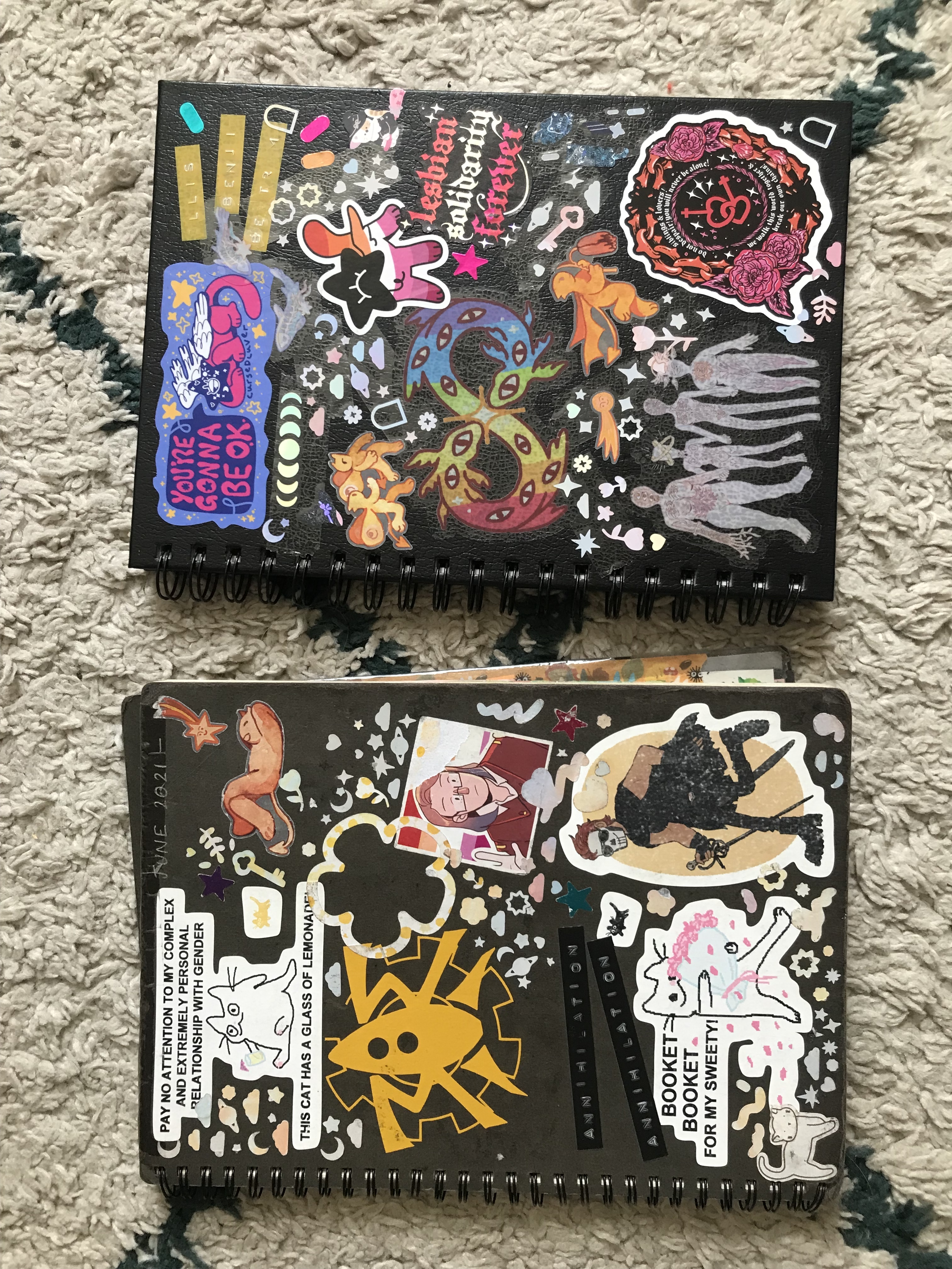 Two black sketchbooks, one older and one brand new, covered in stickers.