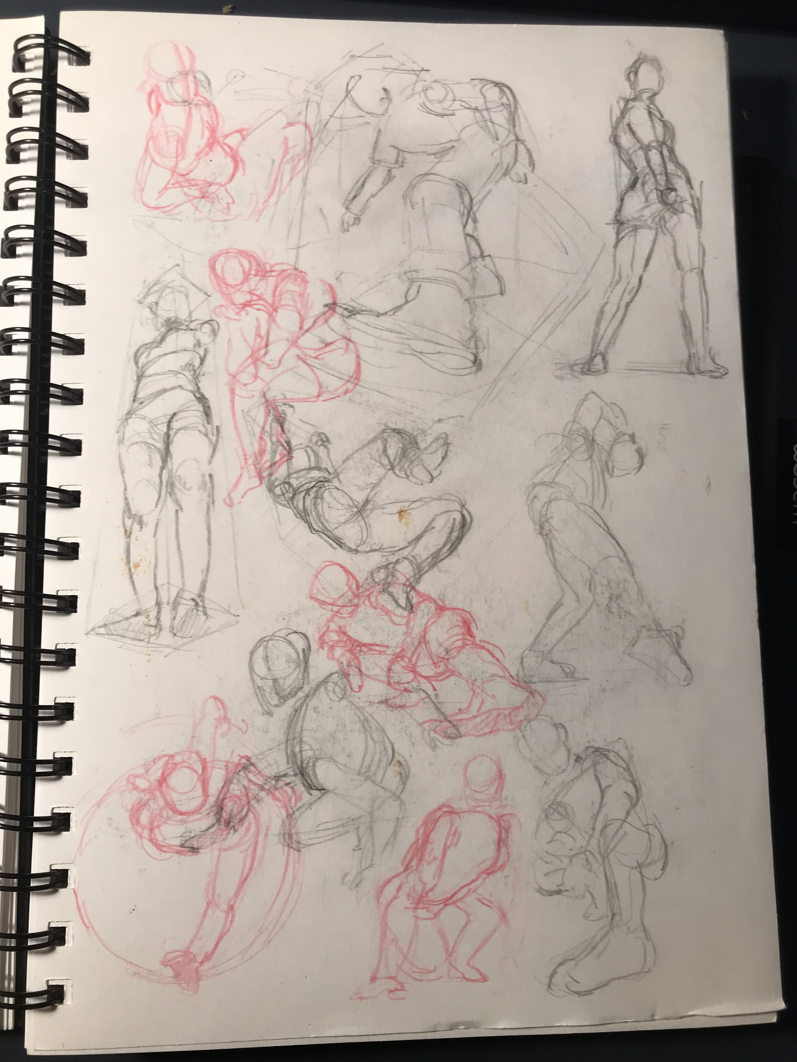 A photo of a sketchbook page of sketches of human bodies in perspective in graphite and red mechanical pencil.