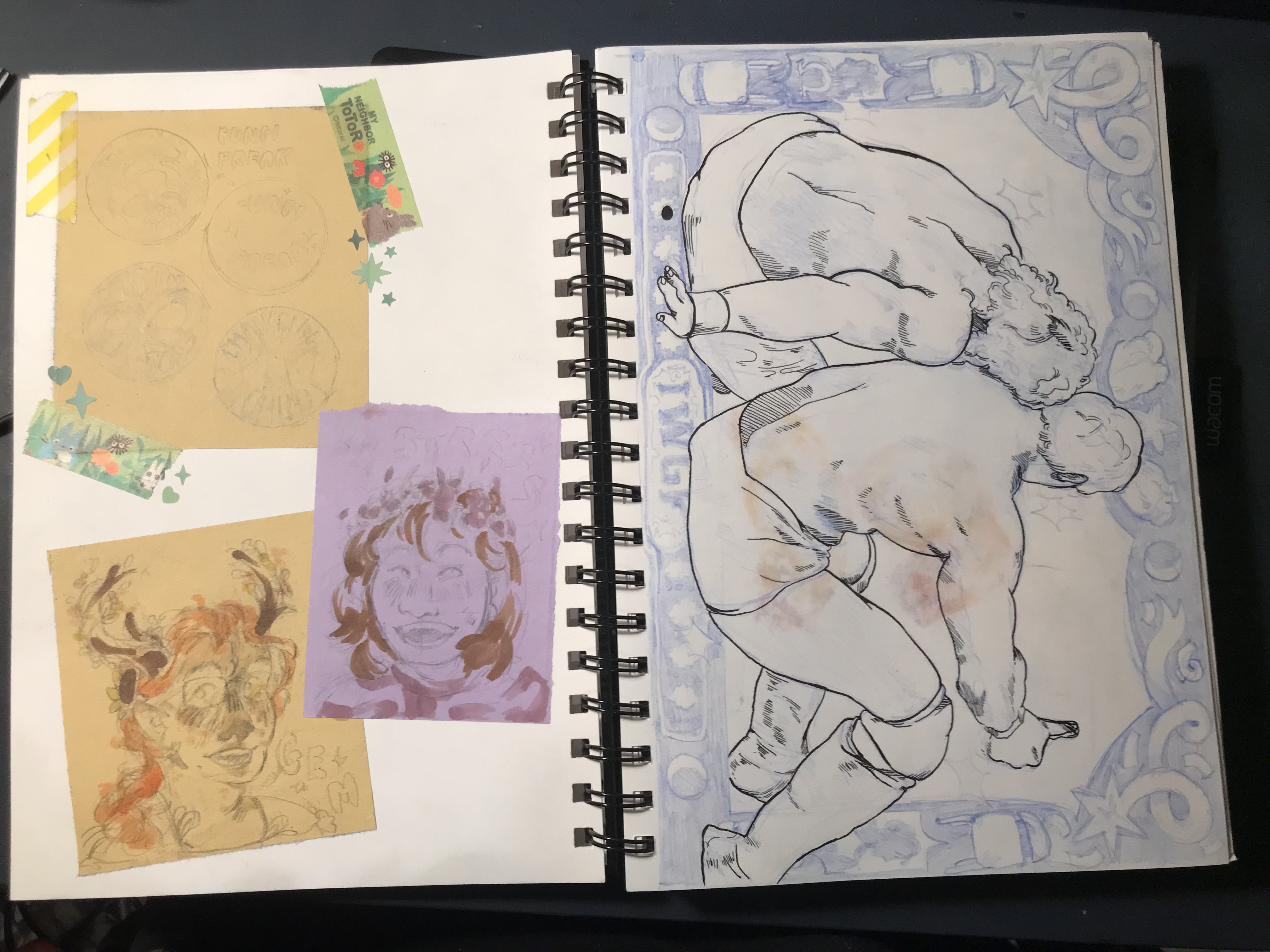 A photo of two pages in a sketchbook, one with cut out coloured paper taped into the page that contains badge sketches and roughly coloured bust drawings, and the other page has a landscape drawing of the Golden Lovers, two wrestlers, with a decorative frame around the edge, in blue pencil.