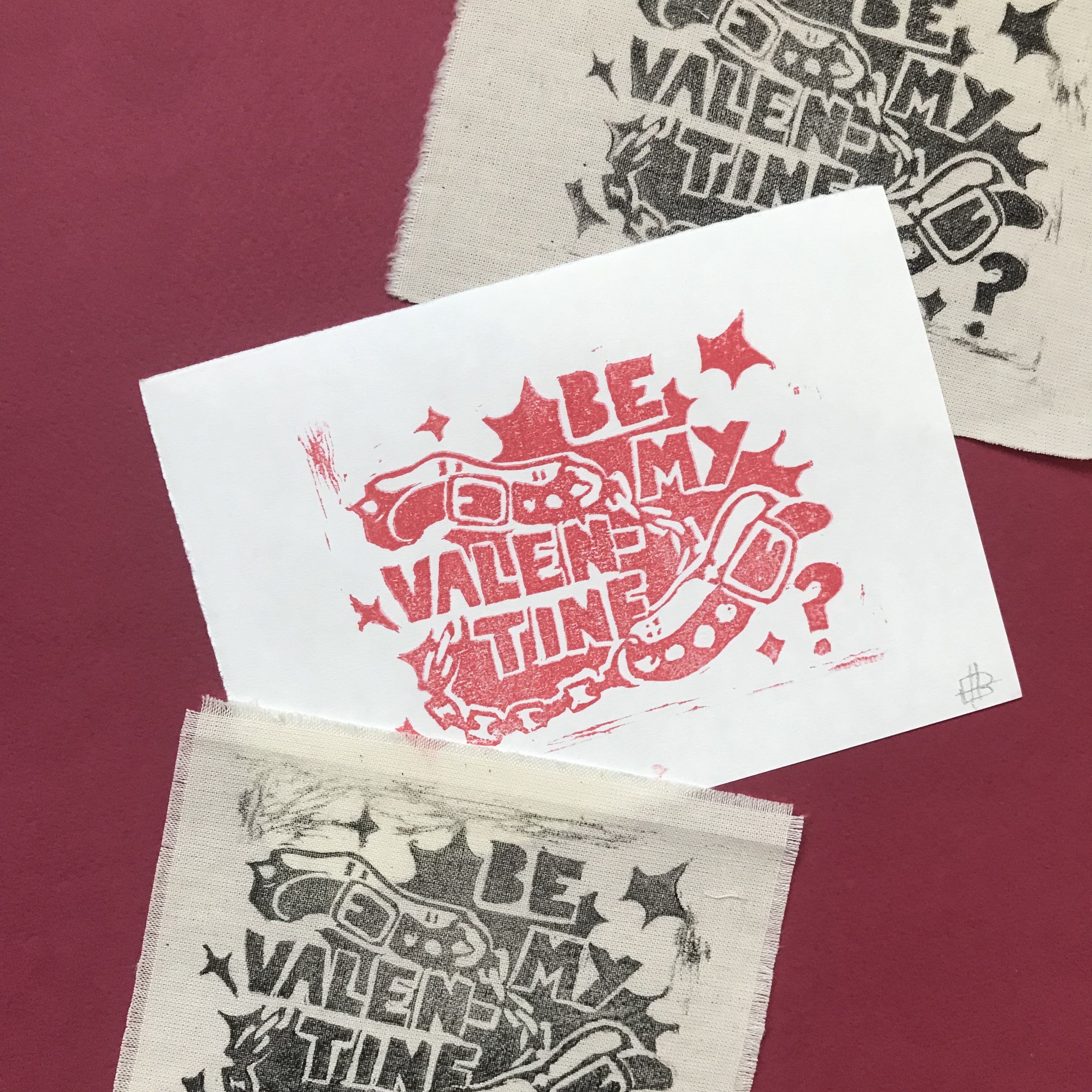 A product photo of a scattered pile of linoprints in black, and at the top, the same design on red against white paper. The design is of two spiked collars tied together, with text in front of them reading 'BE MY VALENTINE.'