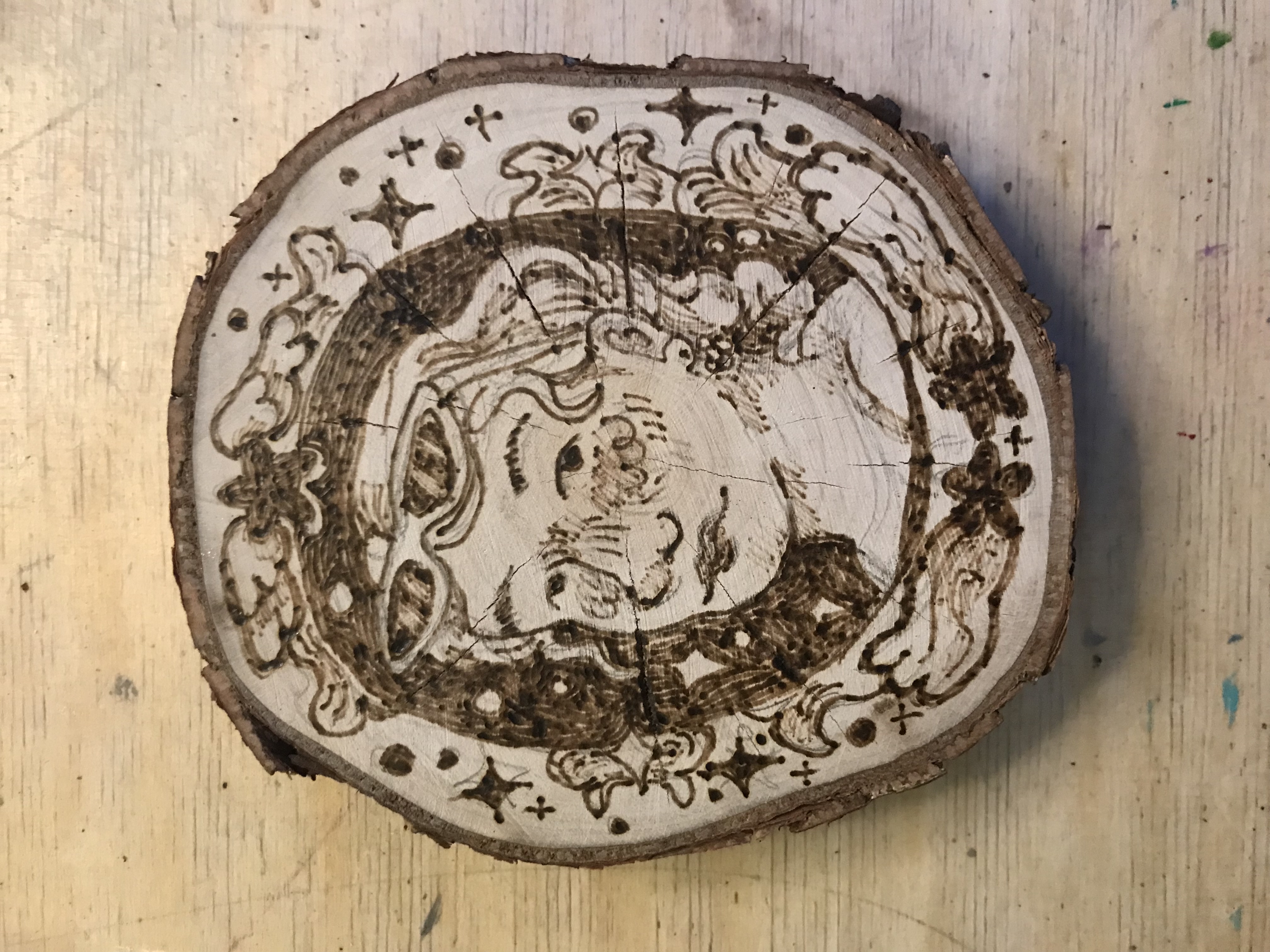 Woodburnt portrait of a person with wavy hair and cat eye sunglasses on top of their head, surrounded by shooting stars and frame like curving shapes.