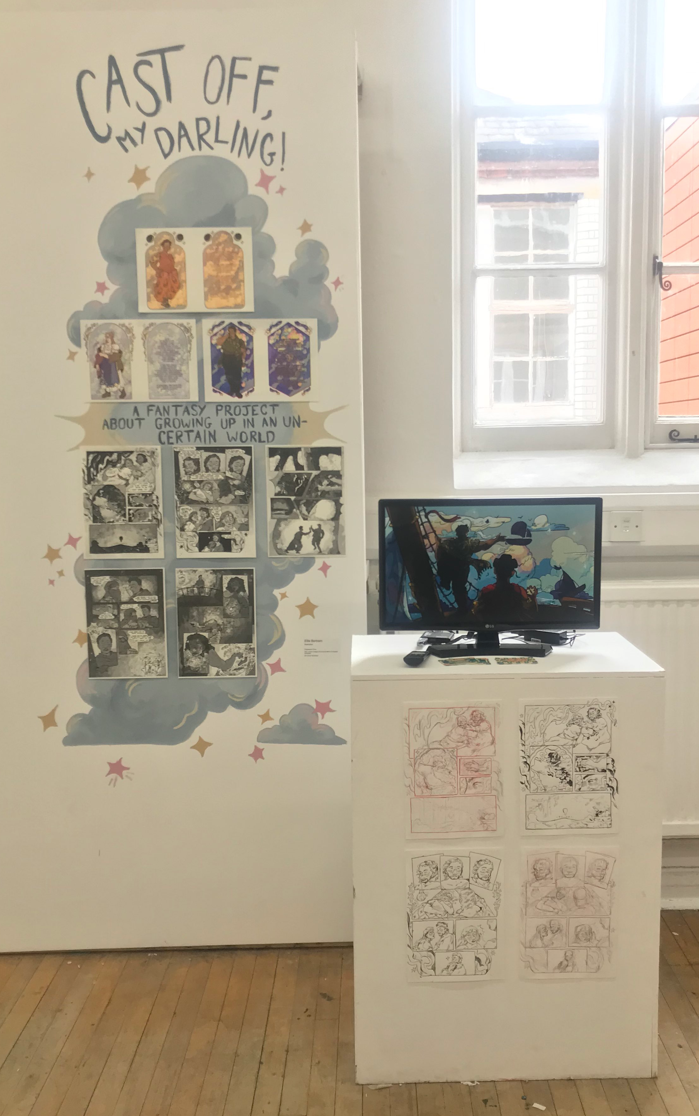 A display of artwork in a show. There are multiple full-colour and black and white risoprints, as well as a tv screen on a plinth playing an animation, which multiple sketches are displayed on the front side of.